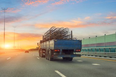 Truck with long trailer loaded with metal cylinder rebar frame for the construction of a building drives along the highway clipart