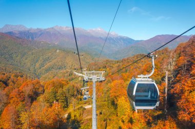 Asansörlerdeki kabinler, sonbahar mevsiminin etrafındaki dağlara kadar uzanır. Dağların yamaçlarında parlak sarı yapraklar vardır.