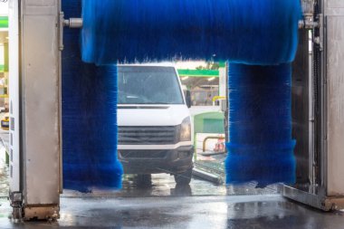 Mavi fırça otomatik olarak hareket halinde, beyaz mini minibüs temiz olarak çıkıyor..