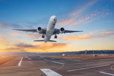 Havaalanı pistinden hızla havalanan ticari uçak, güzel bir günbatımı bulutu manzarasının arka planına doğru ilerliyor.