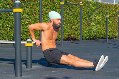 Bandanalı kaslı bir adam, bankta şınav, dışarıda trisepsler. Fitness antrenmanı, spor, kol kasları, şınav.