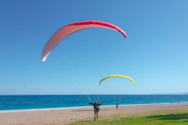 İki insan paraşütçü deniz kıyısında hafif bir meltem rüzgârında havalanmaya hazırlanıyor.