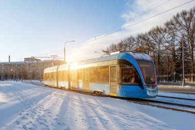 Mavi tramvay, güneşin ışık efektinin kışın yansımasıyla şehirde hızla ilerler.