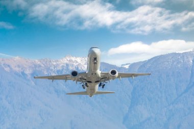 Yolcu jet uçağı, arka planda bulutlu mavi gökyüzü olan bir dağ sırasına doğru hızla havalanıyor..