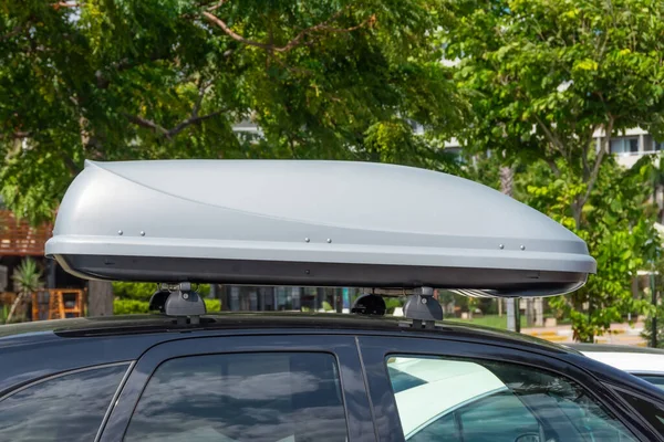 Black plastic car rooftop cargo box or roof carrier for traveling. Removable storage container mounted on car roof rack.