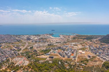 Tepe dağları üzerinden uçuş çalılarla kayalık arazi, şehre bakan kuş bakışı manzara, evler ve binalar, yollar ve gemiler, Akdeniz kıyıları, tatil bölgesi, tatil gezisi