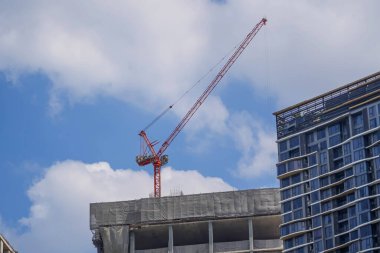 Beyaz bulutlu mavi gökyüzünün arka planında kule vinçleri ve tamamlanmamış binalar. Konut inşaatı, şehirdeki apartmanlar.