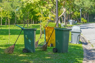 Şehir parkında yeşil sarı çöp tenekesi ve süpürge