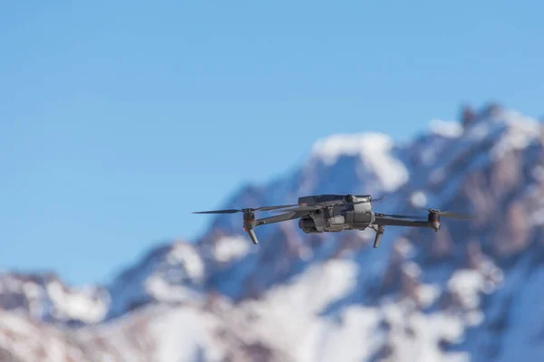 Drone with digital camera flying over winter landscape with snow covered mountains and trees. White remote controlled hovering above snowy mountain peak. Close up shot of drone uav