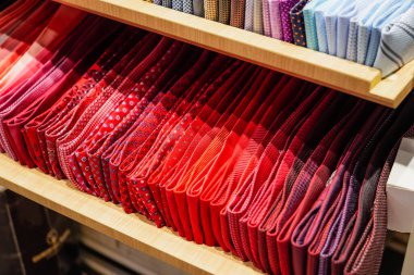 Katı tasarım desenli kırmızı tonlu ve sıcak tonlu kravatlar şık erkek giyim mağazasının vitrininde sıra sıra katlanır.