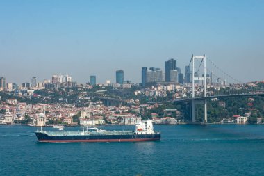 Kargo gemisi İstanbul şehri ve gökdelenleriyle birlikte İstanbul Boğazı boyunca bir köprünün altından geçiyor..