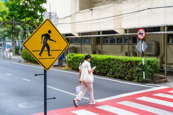 Pedestrian woman crosses the road on a red and white striped pedestrian crossing in an urban environment with a yellow sign.