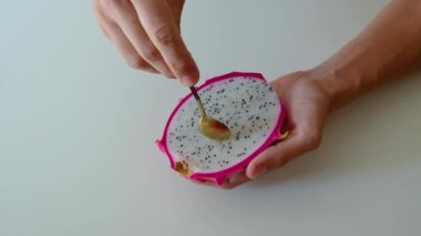 Adam kaşığı eliyle tutuyor, ejderha meyvesi yiyor, güzel bir şekilde yuvarlak parçalar çıkarıyor, meyve dilimleri.