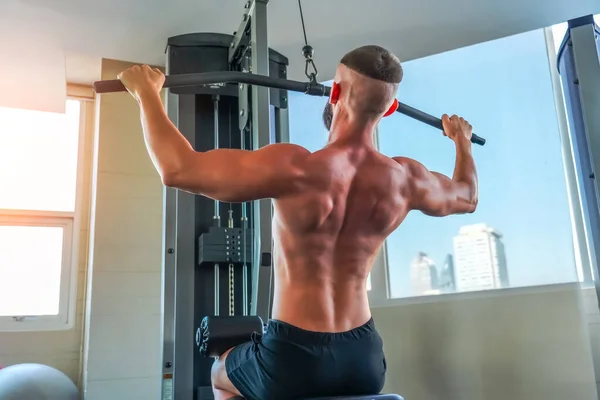 Strong man pulling a vertical upper block, doing back exercises in a modern gym