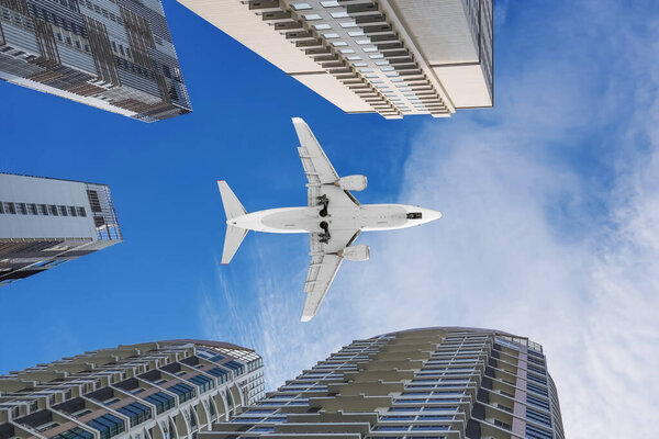 Airplane jet flying above in the sky among tall buildings in a modern office metropolis. Look up into the sky