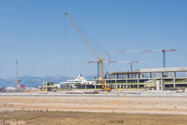 Construction of a new airport terminal building, view of cranes machinery and aircraft parked around. Transport hub reconstruction