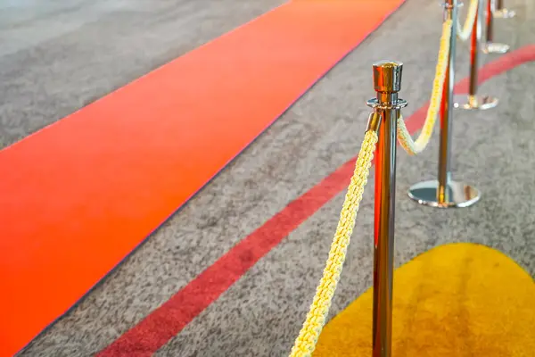 Rope fencing with gold pillars with a red carpet for celebrities and guests of an expensive event with crowds of people
