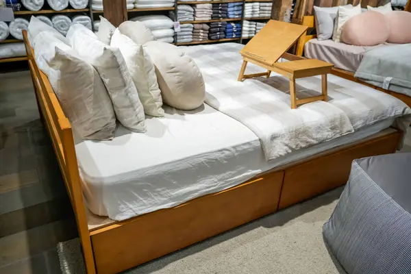 Double beds with glazed linens, duvet, sheets and pillows in furniture store. Table for bed eat food morning breakfast.