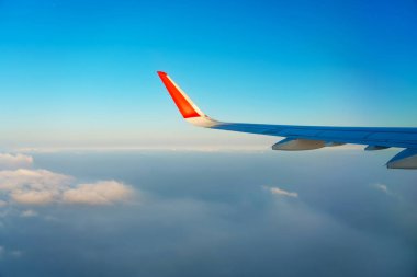 Uçak penceresinden bulutlara ve günbatımına kadar olan manzara. Kalın açık mavi eğimli gökyüzünün üzerinde bir uçak kanadı. Harika nefes kesici manzara