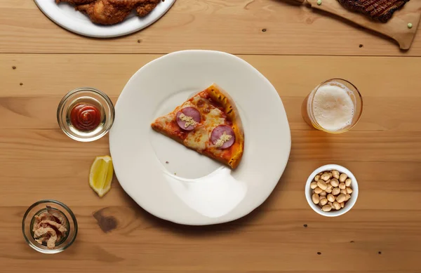 木制餐桌 各种食物 享受欢乐时光 主菜披萨 烤牛肉 花生和一杯啤酒 顶视图 图库照片