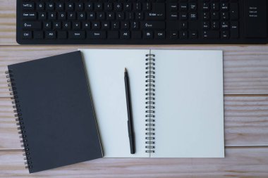 Siyah bilgisayar klavyesi, kalem ve not defteri olan ofis masasının tam üstünde.
