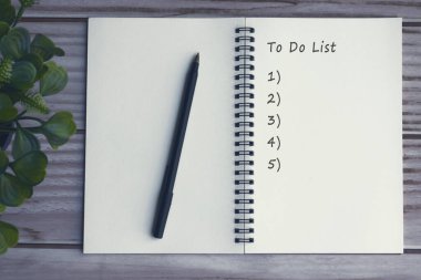 Ahşap masa ve saksı bitkisi ile sözcükleri listelemek için kalem ve defter.