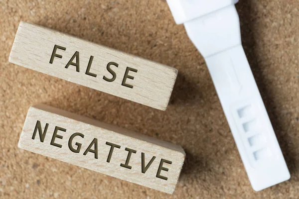 False negative words on wooden block with pregnancy test kit.