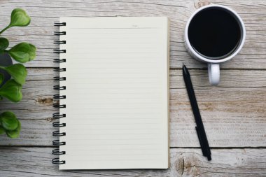 Kalem, not defteri, bitki ve kahvenin olduğu bir masanın tam üstünde. Düz yatıyordu. Boşluğu kopyala.