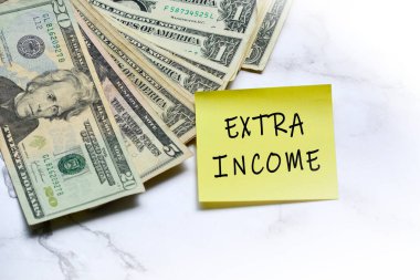 Dolarlar ve yapışkan notlar. Masanın üzerine de ExTRA Gelirleri yazılmış. Ekstra para kazanma kavramı.