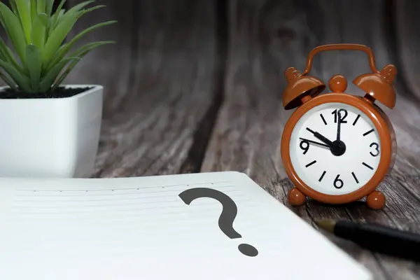 Question mark on notepad alarm clock on wooden background. Q and A concept.