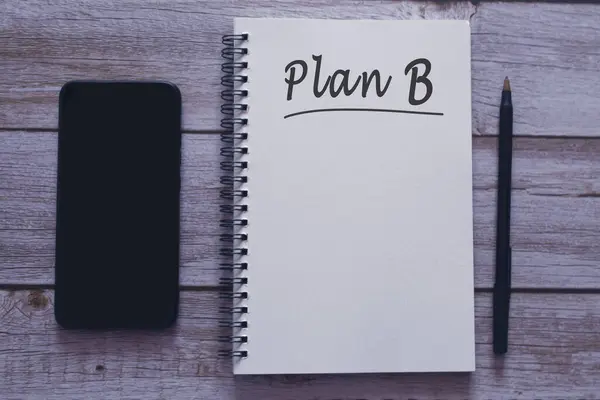 Plan B written on notepad with smartphone and pen on wooden desk. Backup plan concept.