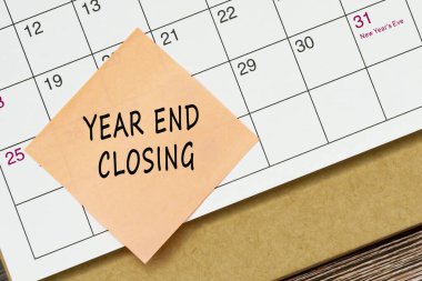 Yıl sonu kapanış metni turuncu kağıt yapışkan not ve takvim arka planına yapışmış. Hatırlatma ve denetim kavramı.