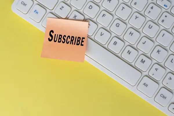 Subscribe text on orange sticky note on top of white keyboard. Social media marketing concept background.