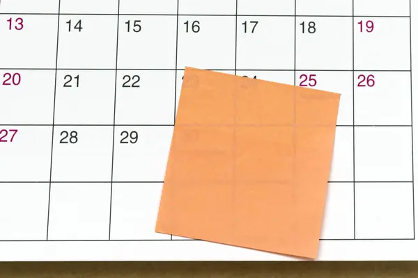 Orange paper sticky note on calendar. Copy space. Flat lay.