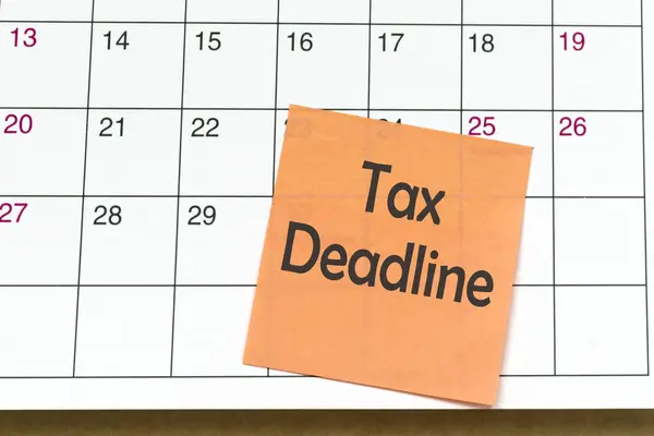 Tax deadline text on orange paper sticky note and stuck to a calendar background. Tax season concept.