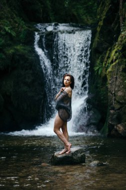 Ormandaki dağ nehrinin yanındaki kayada oturan güzel genç bir kadın. Yüksek kalite fotoğraf