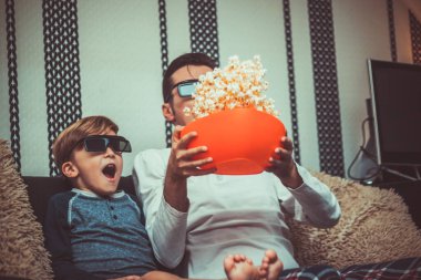 Shocked son and father watching 3D movie and having fun with popcorn. 