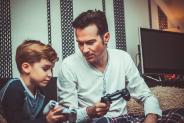 Mid adult father and son talking while playing video games in the living room. 