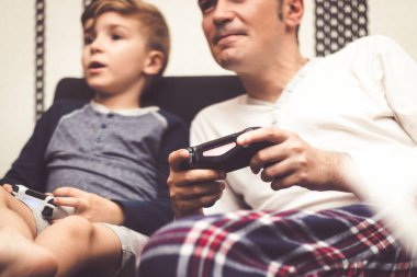 Close up of father and son using game controllers and competing in video game at home. 