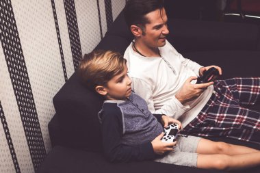 High angle view of father and son playing video games while relaxing on the sofa. 