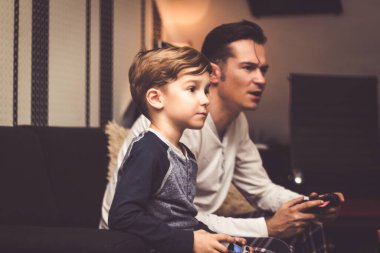 Small kid and his dad playing video game with wireless controllers at home. 