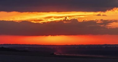 Güneş batarken renkli gökyüzü traktörün zaman aşımına uğramış geniş bir tarımsal alanda.