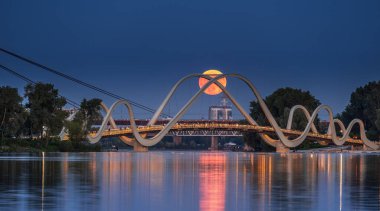 Ukrayna 'nın başkenti Kyiv' deki yaya köprüsünün arkasından pembe çilekli dolunay yükseliyor.