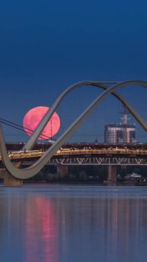 Pembe Çilek Dolunay, Obolon, Ukrayna 'daki yaya köprüsünün arkasından yükseliyor, zaman aşımı, dikey video sstkVertical