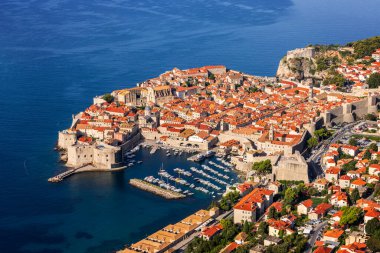 Hırvatistan 'ın Dubrovnik kentindeki Panorama: kale duvarları, turuncu çatıları ve Adriyatik Denizi kıyısında bir marinası olan tarihi eski bir kasaba. Tepeler ve yemyeşil yeşilliklerle çevrili.