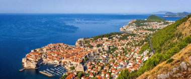 Hırvatistan 'ın Dubrovnik kentindeki Panorama: kale duvarları, turuncu çatıları ve Adriyatik Denizi kıyısında bir marinası olan tarihi eski bir kasaba. Tepeler ve yemyeşil yeşilliklerle çevrili.
