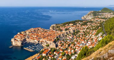 Hırvatistan 'ın Dubrovnik kentindeki Panorama: kale duvarları, turuncu çatıları ve Adriyatik Denizi kıyısında bir marinası olan tarihi eski bir kasaba. Tepeler ve yemyeşil yeşilliklerle çevrili.