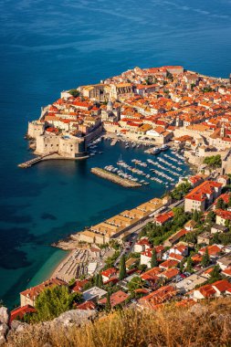 Hırvatistan 'ın Dubrovnik kentindeki Panorama: kale duvarları, turuncu çatıları ve Adriyatik Denizi kıyısında bir marinası olan tarihi eski bir kasaba. Tepeler ve yemyeşil yeşilliklerle çevrili.