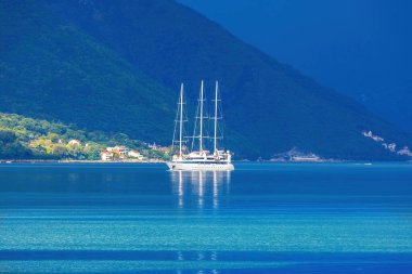 Karadağ 'ın Perast kentinde sabahın erken saatlerinde çekilmiş bir fotoğraf. Güneş ışığının ilk ışıkları çan kulesini aydınlatarak gölgeli dağlara ve derin mavi sulara çarpıcı bir kontrast oluşturuyor..