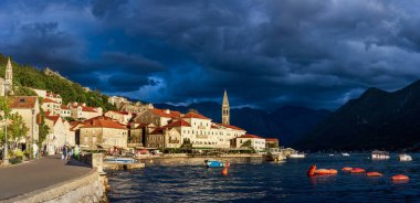 Karadağ 'ın eski Perast kenti, fırtınadan önce gün batımında. Kırmızı çatıları olan taş evler, bir kilise kulesi ve sakin sular dağlar ve güneş ışığıyla sakin bir manzara yaratır. 